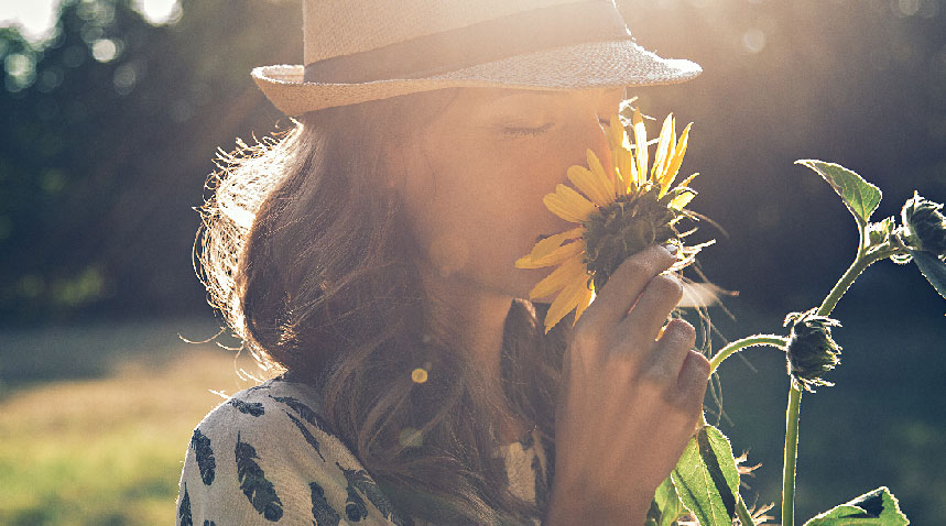 A woman smelling a sunflower under the sun